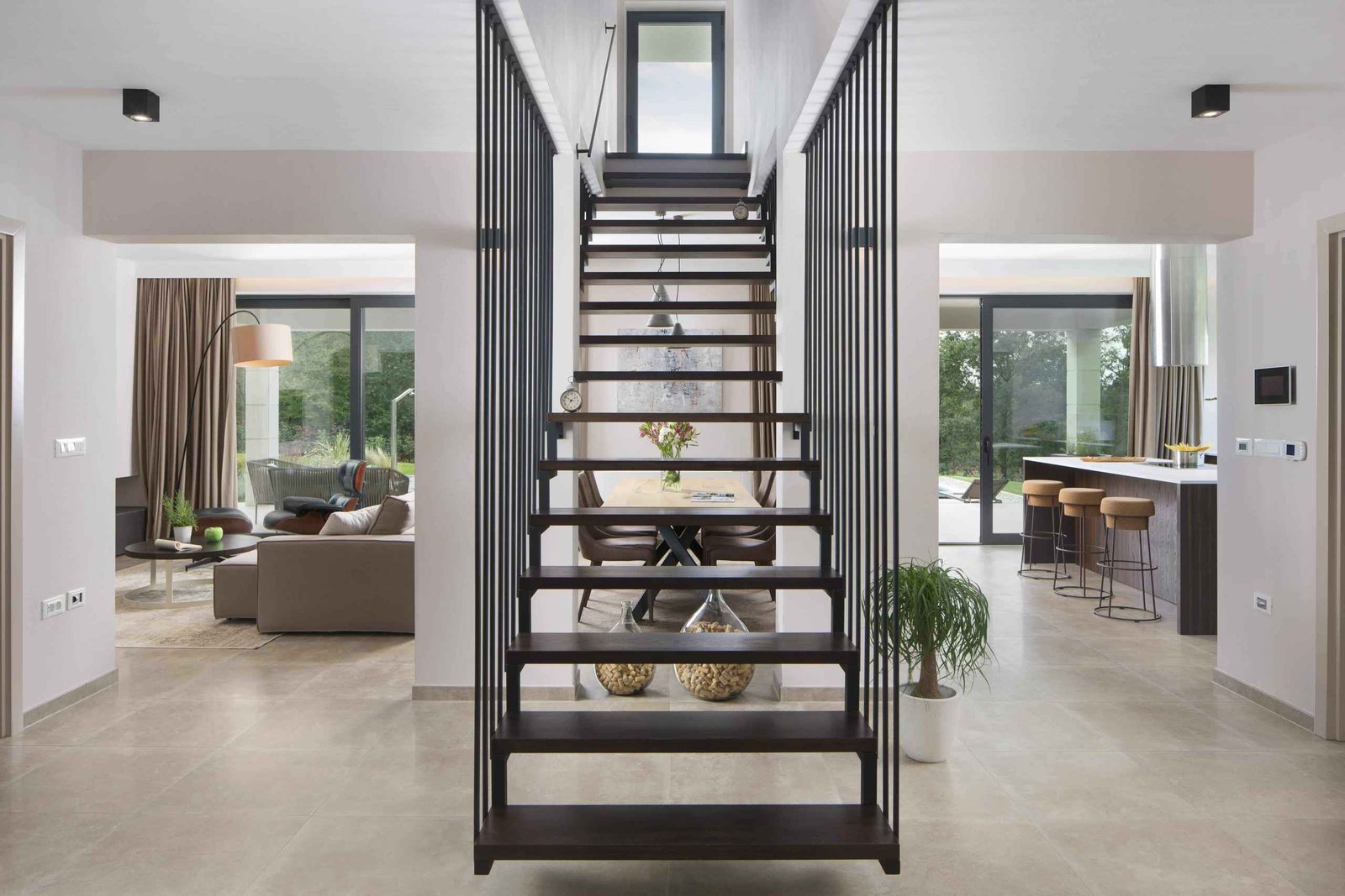 Modern interior of a spacious home with sleek metal stairs leading to the upper level, large windows, and an open-plan living area with minimalist decor.